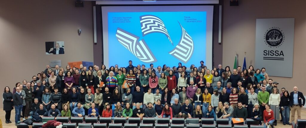 Partecipanti al Convegno Nazionale di Comunicazione della Scienza riuniti in aula davanti a schermo con logo dell'evento